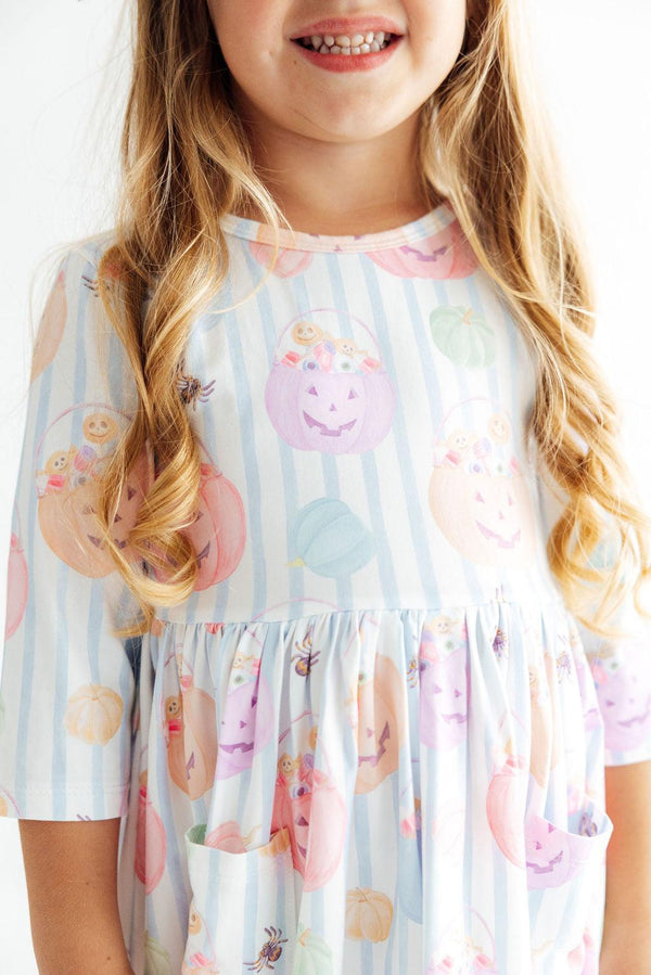 Girl wearing Here for the Candy 3/4 sleeve pocket twirl dress with pastel stripes and pumpkin candy print.