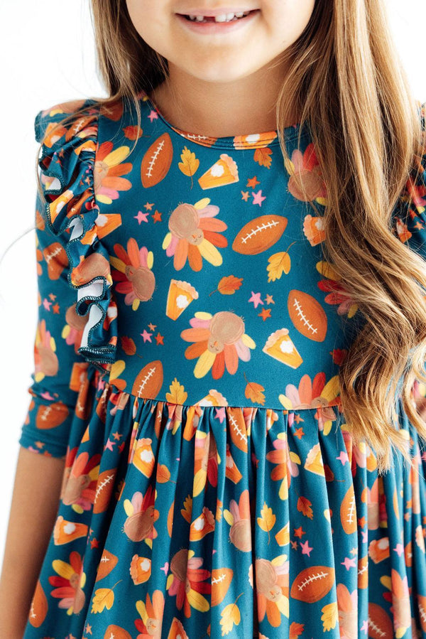 Gobble til You Wobble 3/4 sleeve ruffle twirl dress on a girl; teal print with flowers and footballs, full twirl skirt.