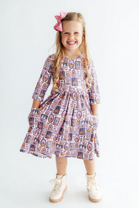 Smiling girl wearing a purple 3/4 sleeve pocket twirl dress with Halloween print, featuring pumpkins, ghosts, and spooky designs for play or costumes.