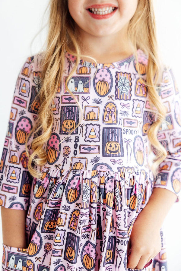 Pink 3/4 sleeve twirl dress with Halloween print featuring pumpkins, ghosts, and "Spooky" text. Includes side pockets for kids.