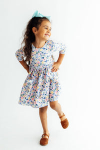 Girl wearing fall floral 3/4-sleeve twirl dress with pockets and turquoise bow, smiling and twirling.