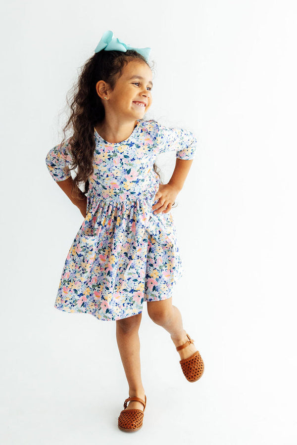 Girl wearing fall floral 3/4-sleeve twirl dress with pockets and turquoise bow, smiling and twirling.