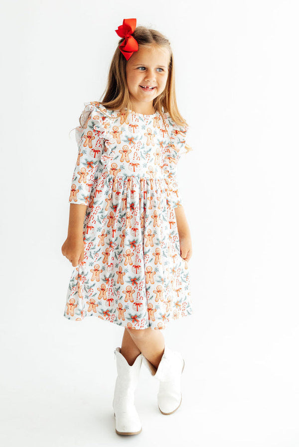 Girl wearing gingerbread print 3/4 sleeve ruffle twirl dress with red bow and white boots for Christmas parties.