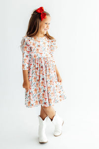 Toddler girl wears white gingerbread print 3/4 sleeve ruffle twirl dress with red bow and white cowboy boots for Christmas.