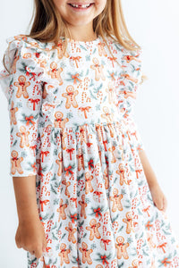 Girl wearing white 3/4 sleeve ruffle twirl dress with gingerbread men, candy canes, and pine print for Christmas.