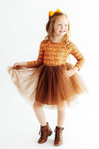 Girl twirling in orange patterned long sleeve tutu dress with brown tulle skirt, orange bow, and brown boots.