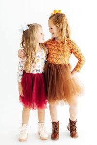 Two girls modeling long sleeve tutu dresses in autumn colors. One features a fall print top with a burgundy tulle skirt, the other has an orange lace bodice with a brown tulle skirt.