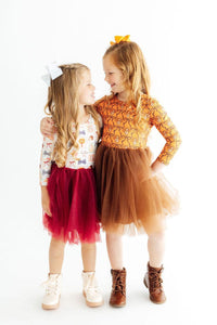Two girls modeling Hello Fall long sleeve tutu dresses. One wears a burgundy tulle skirt with a printed top, the other brown tulle with an orange patterned bodice.