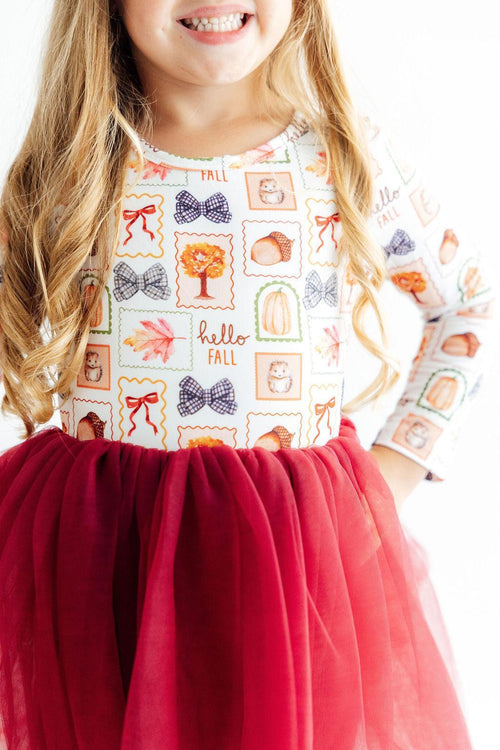 Child wearing fall themed long sleeve dress with autumn print top and red tutu skirt. Perfect ballerina outfit for twirling.