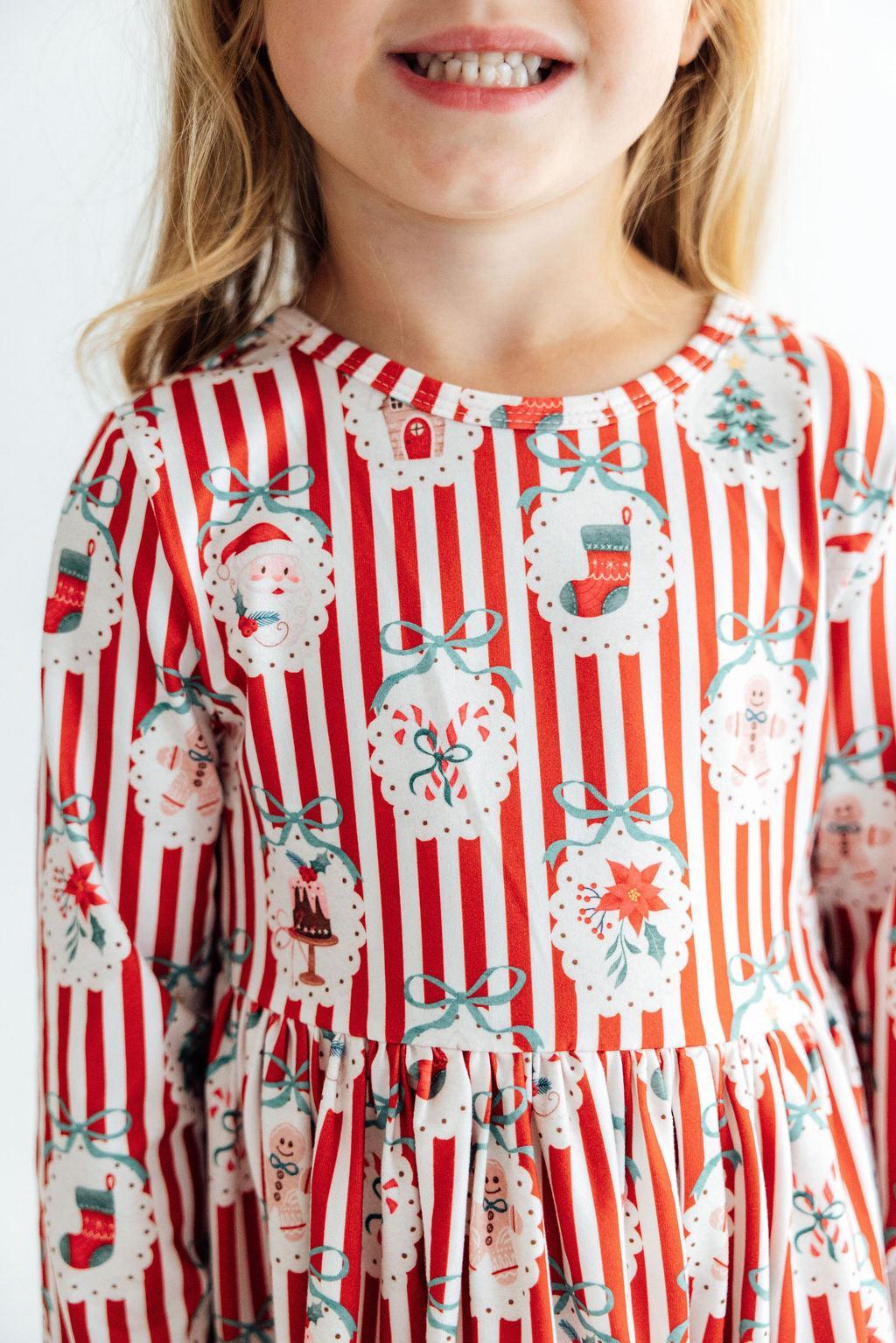 Girl wearing a red and white striped long sleeve dress with Santa, stockings, and bows print and ruffle hem.