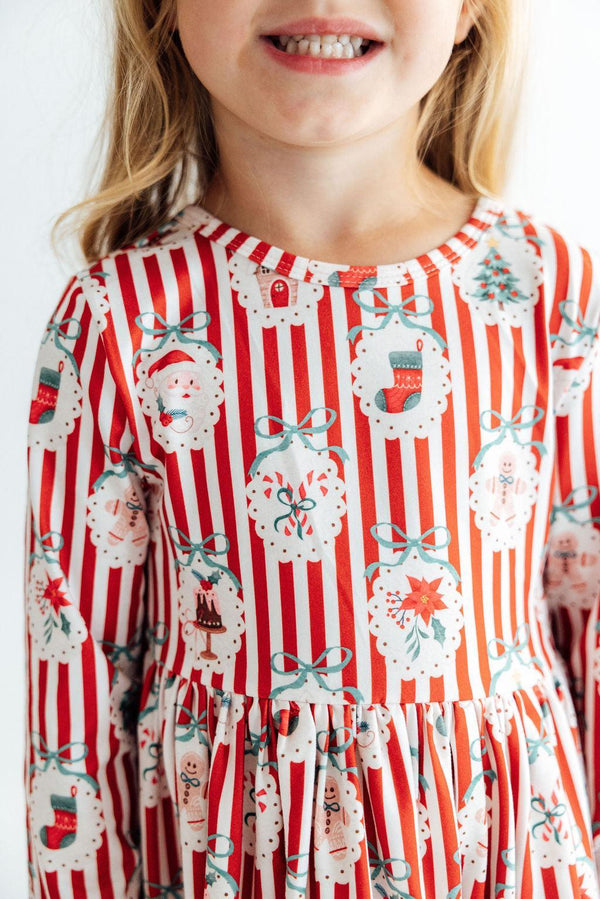 Girl wearing a red and white striped long sleeve dress with Santa, stockings, and bows print and ruffle hem.