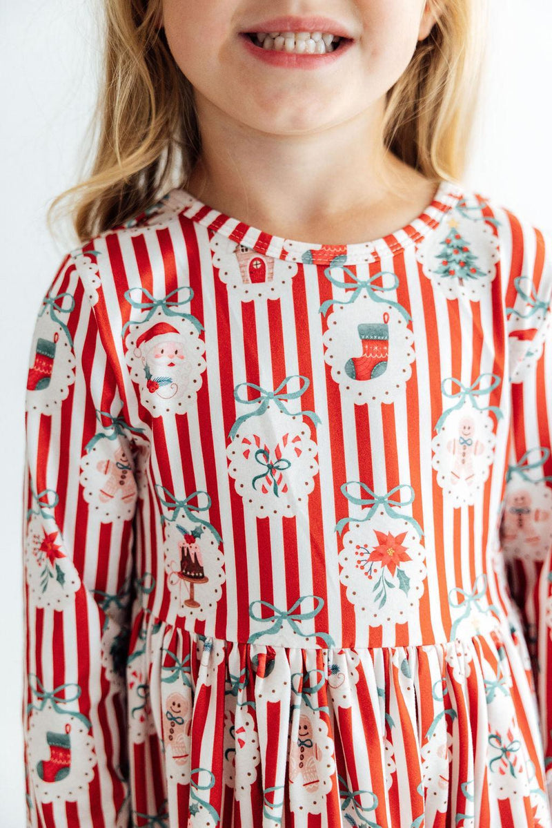 Girl wearing a red and white striped long sleeve dress with Santa, stockings, and bows print and ruffle hem.