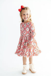 Young girl wearing a red and white striped long sleeve dress with Christmas prints, ruffle hem, and red bow.