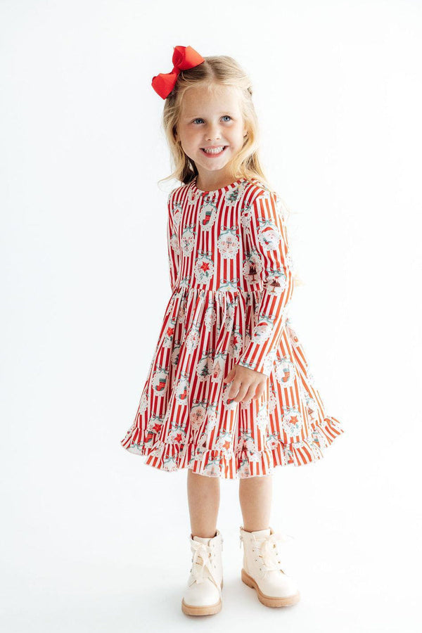 Young girl wearing a red and white striped long sleeve dress with Christmas prints, ruffle hem, and red bow.