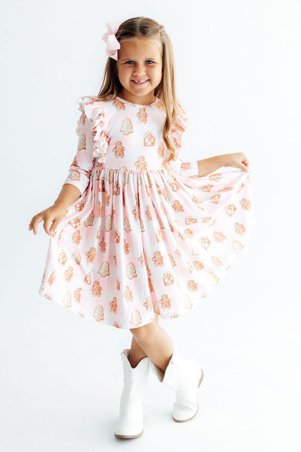 Girl twirling in pink Christmas ruffle dress with gingerbread print and white boots, perfect for holiday parties.