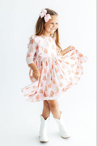 Girl twirling in pink 3/4 sleeve ruffle dress with gingerbread print and white cowboy boots. Perfect Christmas party outfit.