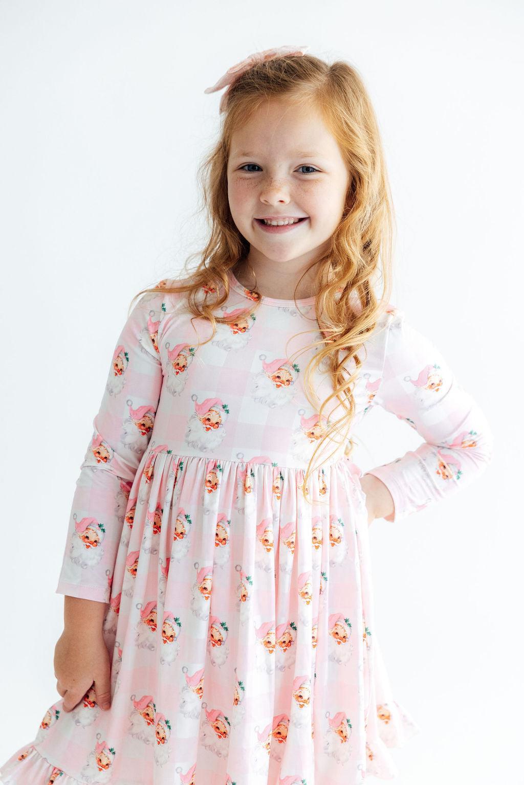 Girl wearing pink gingham Storybook Santa long sleeve dress with ruffle hem and full skirt for twirling.