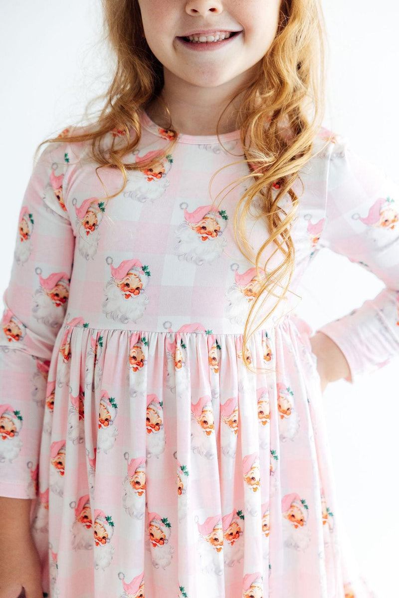 Girl wearing pink gingham long sleeve twirl dress with vintage Santa print and ruffle hem for special occasions or play.