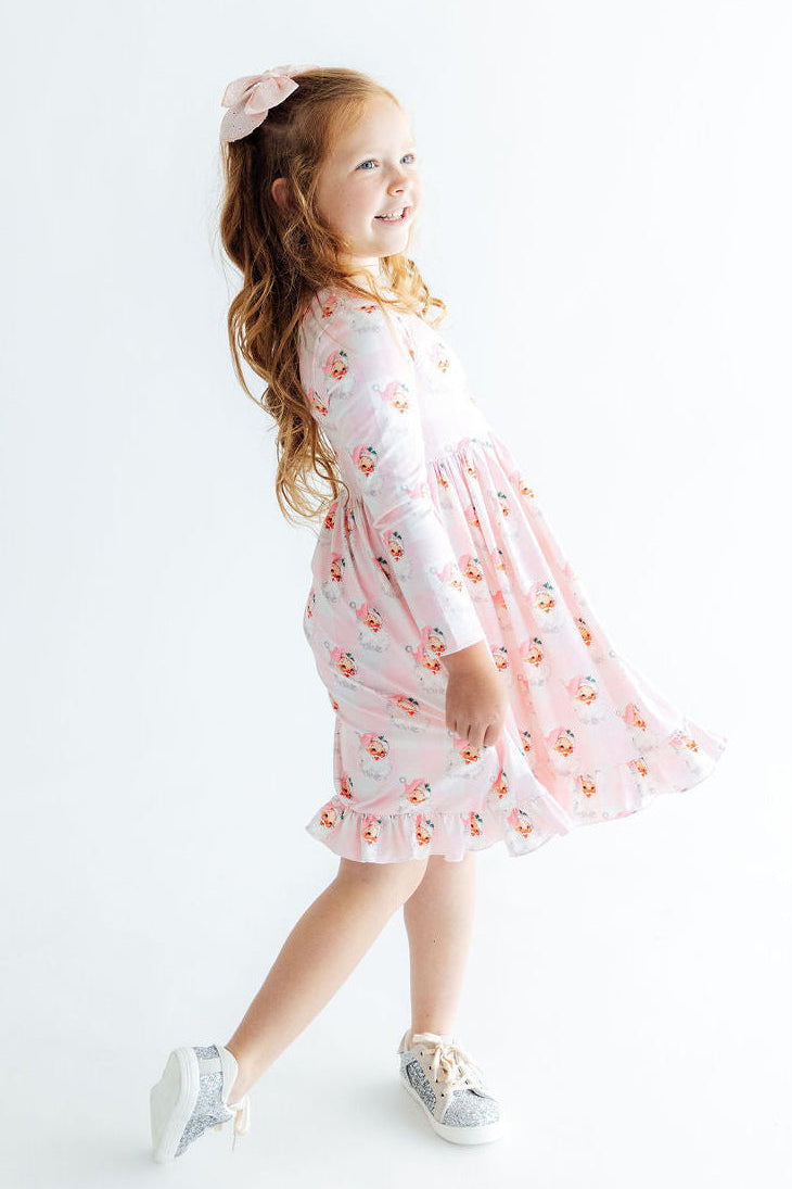 Young girl twirling in a pink Storybook Santa long sleeve ruffle hem dress with sparkly silver sneakers.