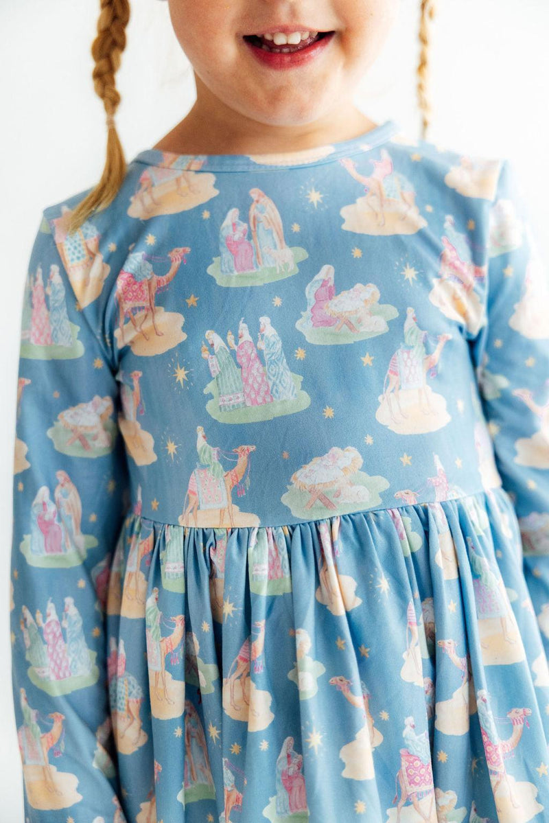 Blue long sleeve twirl dress for girls featuring a nativity print with camels, stars, and ruffle hem. Soft fabric with a full skirt.