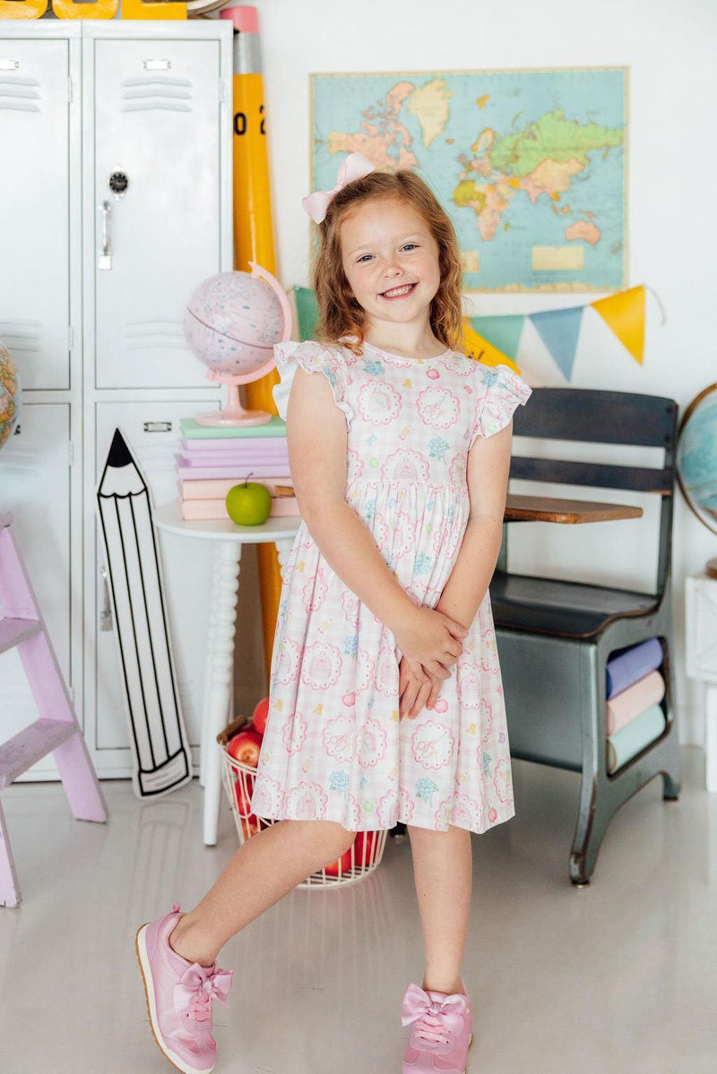 Girl wearing Apple of My Eye Flutter Sleeve Twirl Dress in pastel print, pink sneakers, classroom backdrop.