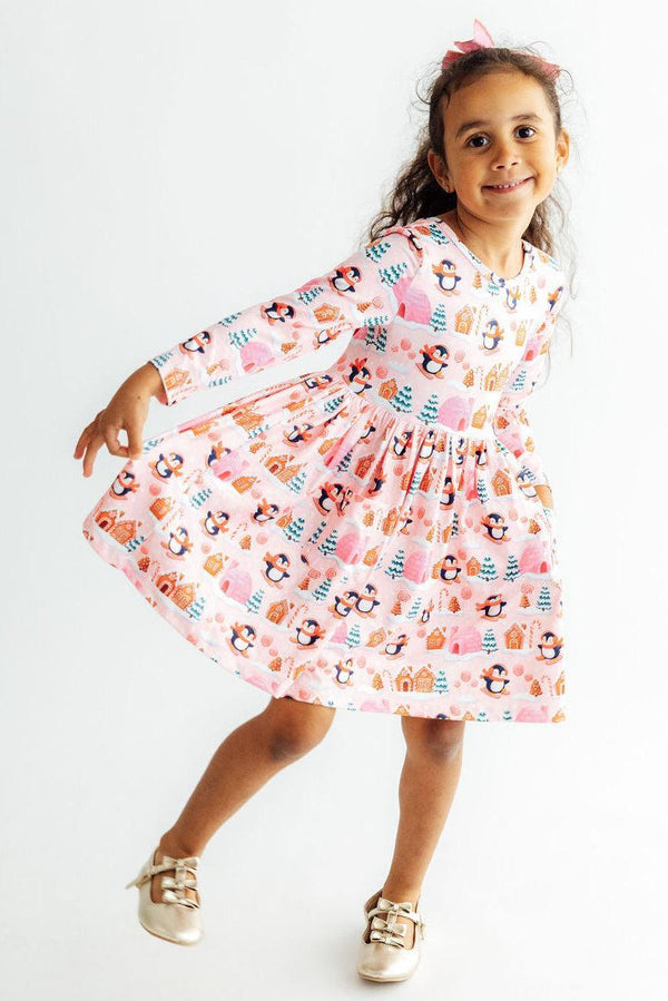 Girl twirling in a pink long sleeve dress with penguin print, full skirt, and ballet neckline for fun play and special occasions.