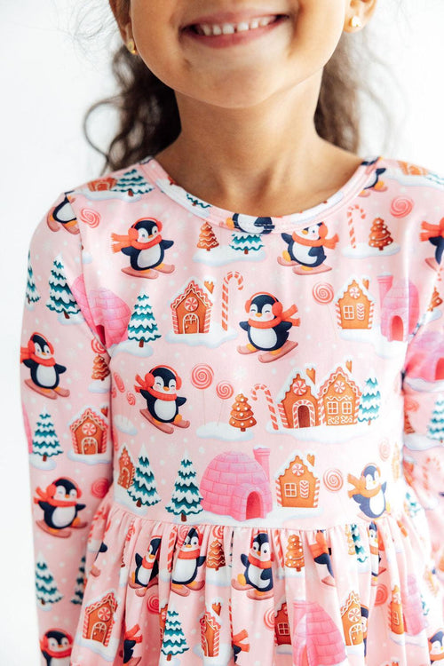 Pink long sleeve twirl dress featuring a festive print of skiing penguins, gingerbread houses, candy canes, and winter trees.