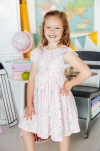 Girl wearing Apple of My Eye Flutter Sleeve Twirl Dress with pastel print, smiling in a classroom.