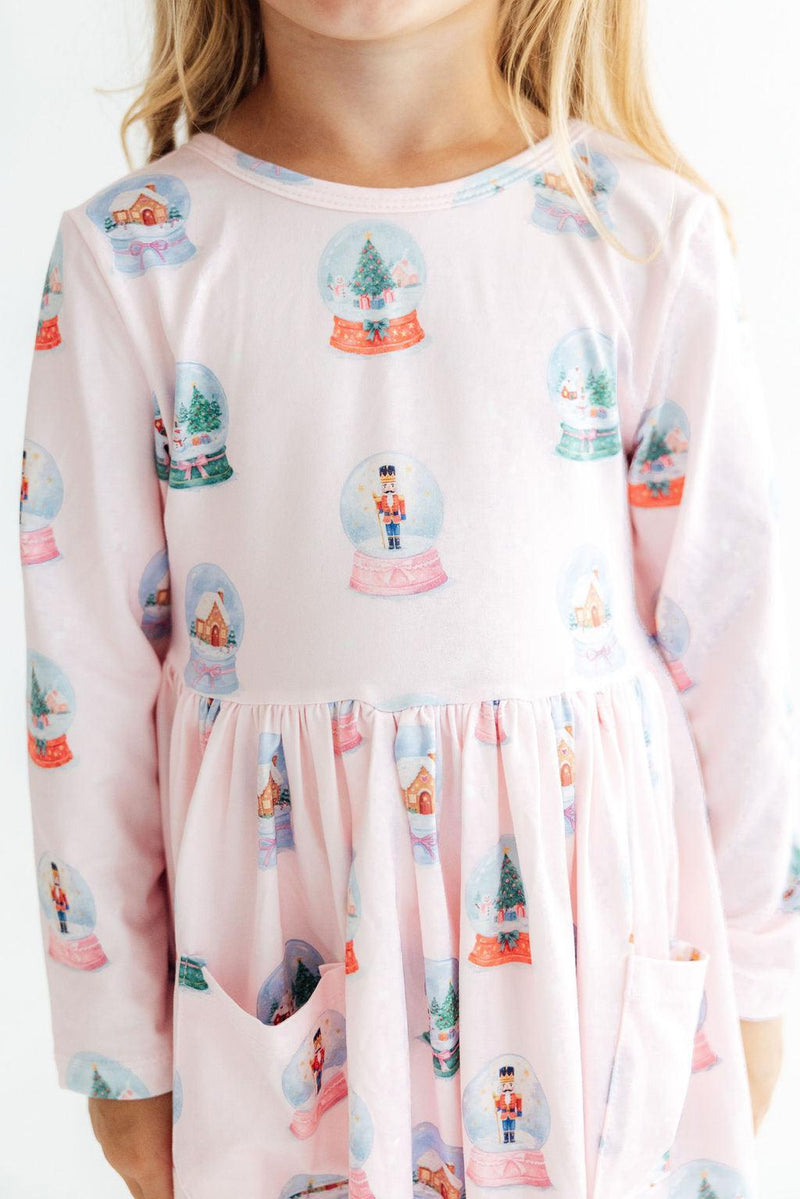 Pink long sleeve twirl dress with festive snow globe print, front pockets, and full skirt. Soft fabric适合school or play.