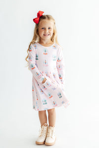 Girl in pink long sleeve snow globe print dress with side pocket and red bow. Perfect twirl dress for school or play.