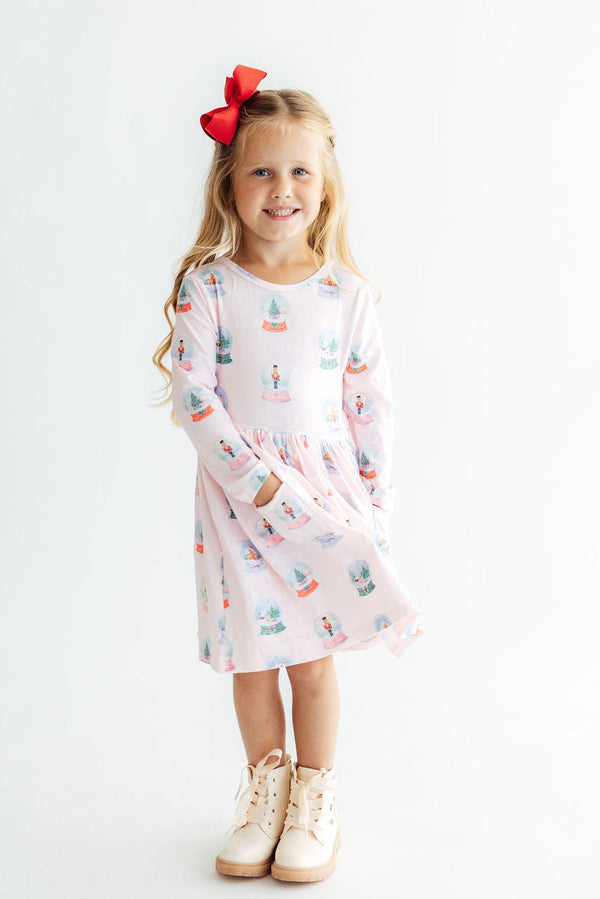 Girl in pink long sleeve snow globe print dress with side pocket and red bow. Perfect twirl dress for school or play.