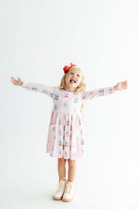 Happy girl twirling in pink long sleeve pocket twirl dress with snow globe print and red bow.