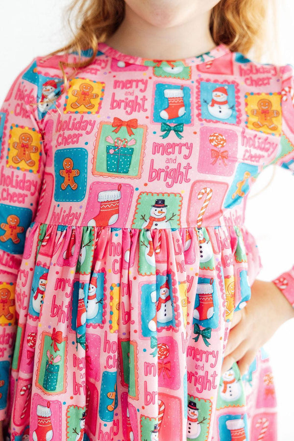 Pink long sleeve girls dress featuring festive snowmen, gingerbread men, and "Holiday Cheer" text on a ruffled twirl skirt.