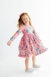 Girl twirling in pink long sleeve ruffle hem dress with festive snowman and gingerbread print.