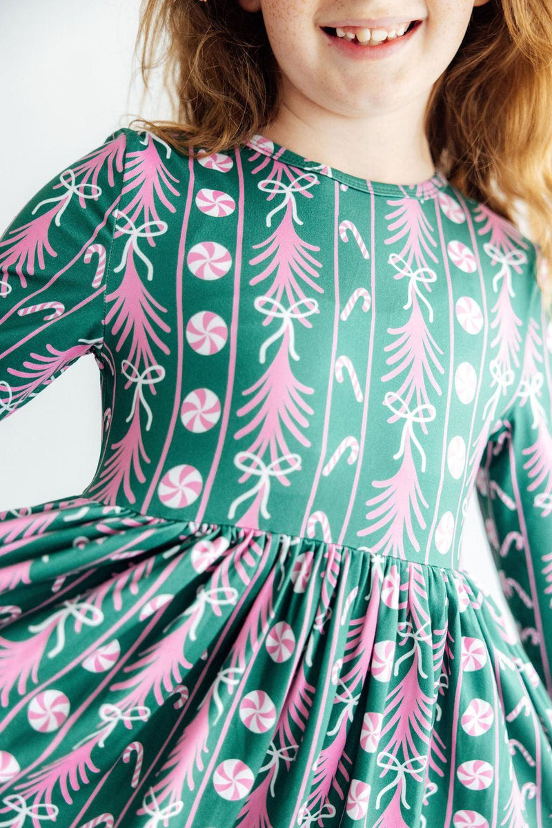 Green long sleeve Christmas dress with pink candy cane and tree print. Features a full ruffle hem for twirling and a comfortable scoop neckline.