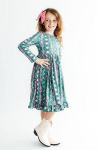 Young girl in Christmas Treats long sleeve twirl dress with teal print, pink accents, ruffle hem and full skirt.