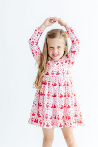 Girl twirling in a long sleeve pink dress with red ballet and nutcracker print, ruffle hem, and full skirt for play.