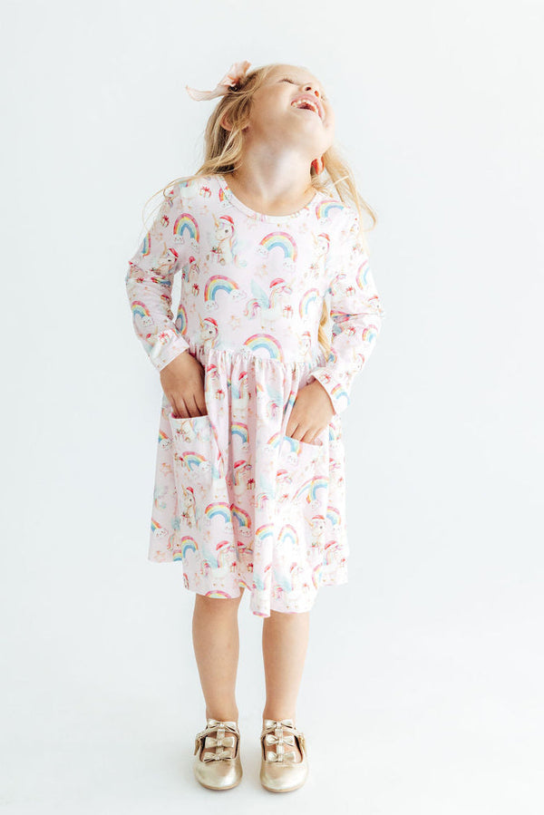 Girl in long sleeve unicorn and rainbow print pocket twirl dress with full skirt and ballet neckline for play.