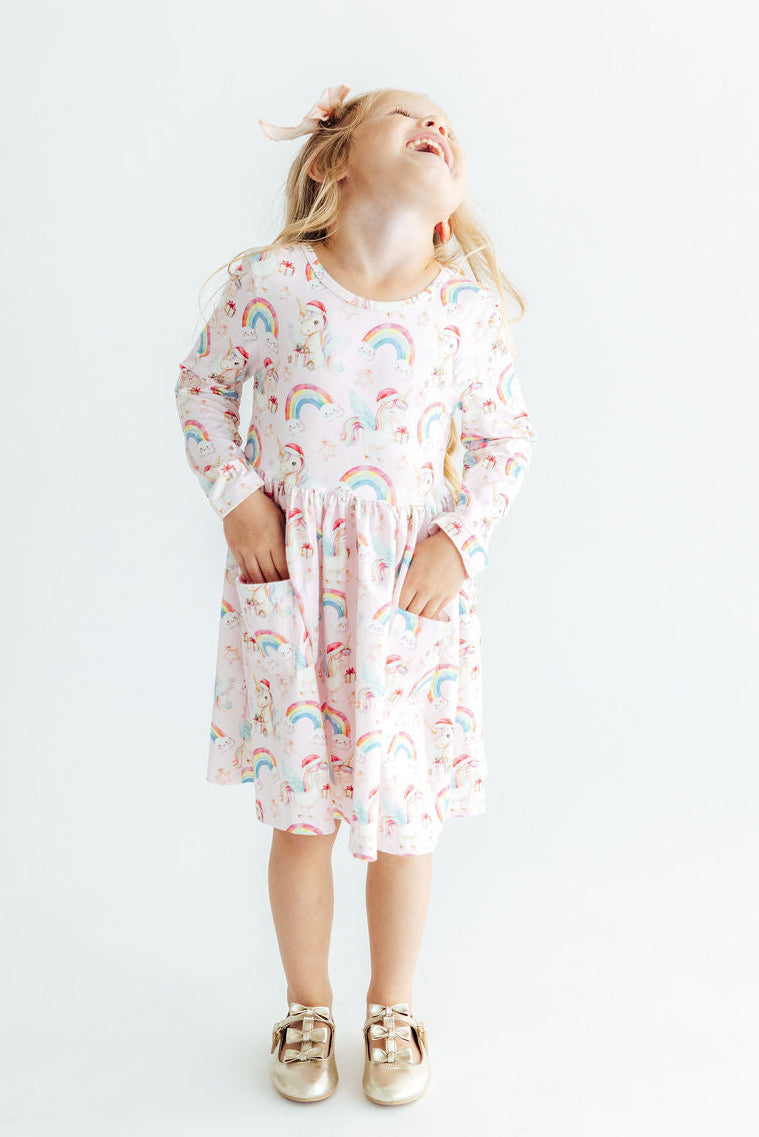 Girl in long sleeve unicorn and rainbow print pocket twirl dress with full skirt and ballet neckline for play.