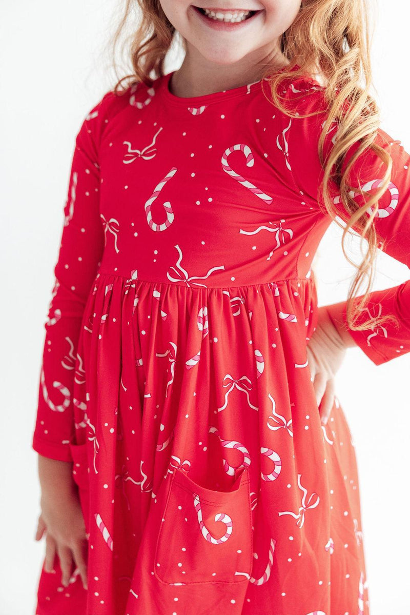 Red long sleeve twirl dress with candy cane print and front pocket. Soft full skirt perfect for school, play, and special occasions.