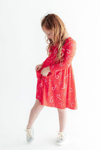 Child in red long sleeve candy cane print twirl dress with front pockets and glitter sneakers.