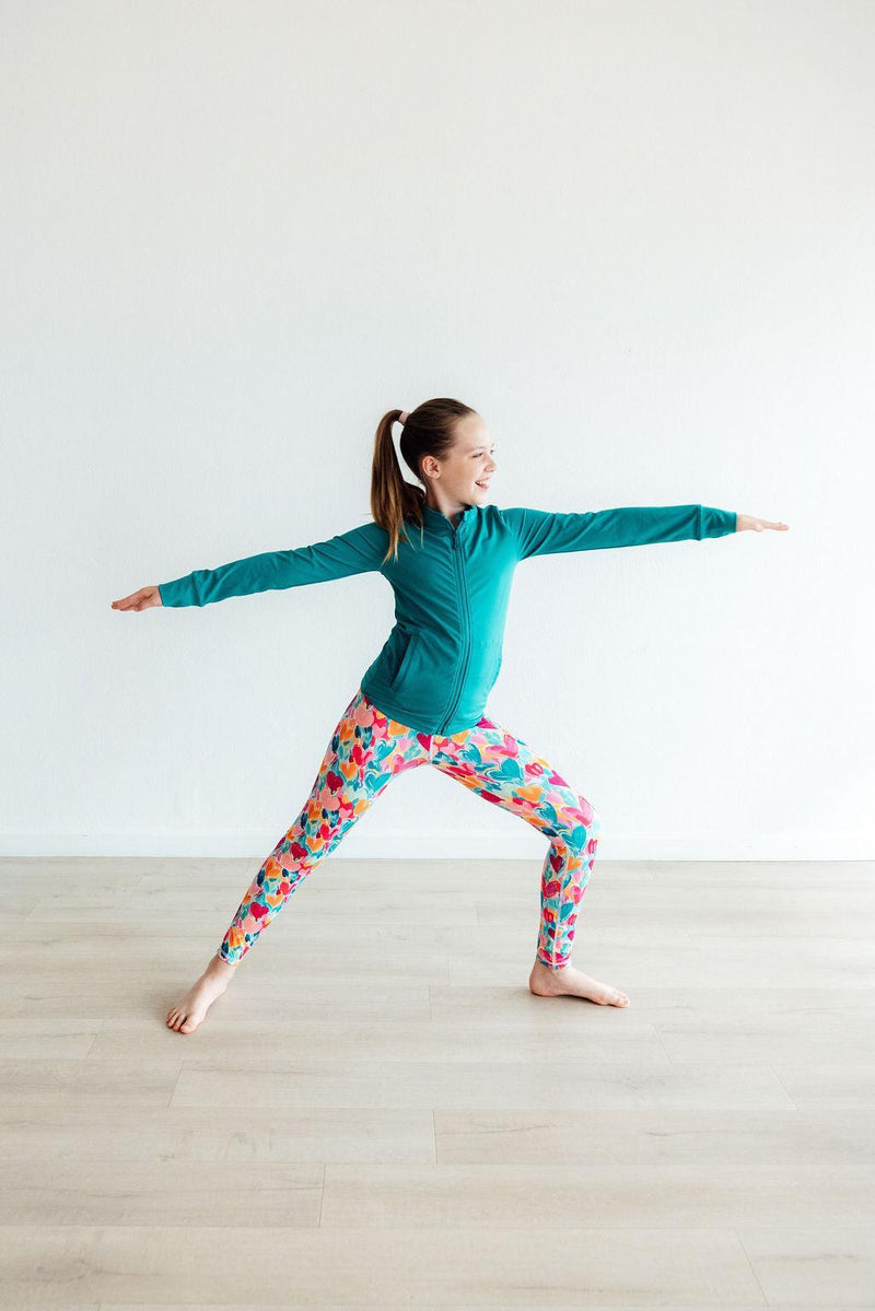Girl in a warrior pose, showcasing the Turbo Teal Full-Zip Ruffle Girls Active Jacket while practicing yoga, part of girls activewear jackets.