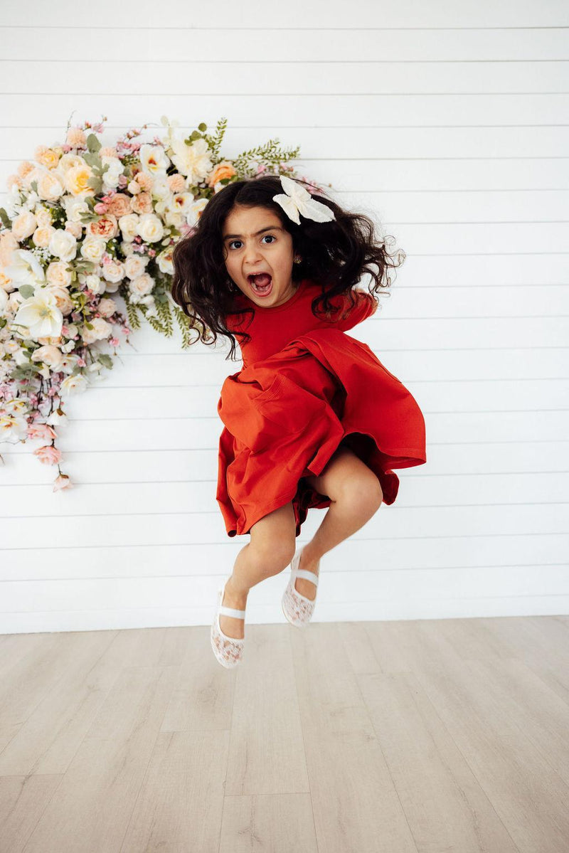 Child joyfully jumping in the Pumpkin Spice 3/4 Sleeve Pocket Twirl Dress, capturing the spirit of playfulness and fun.