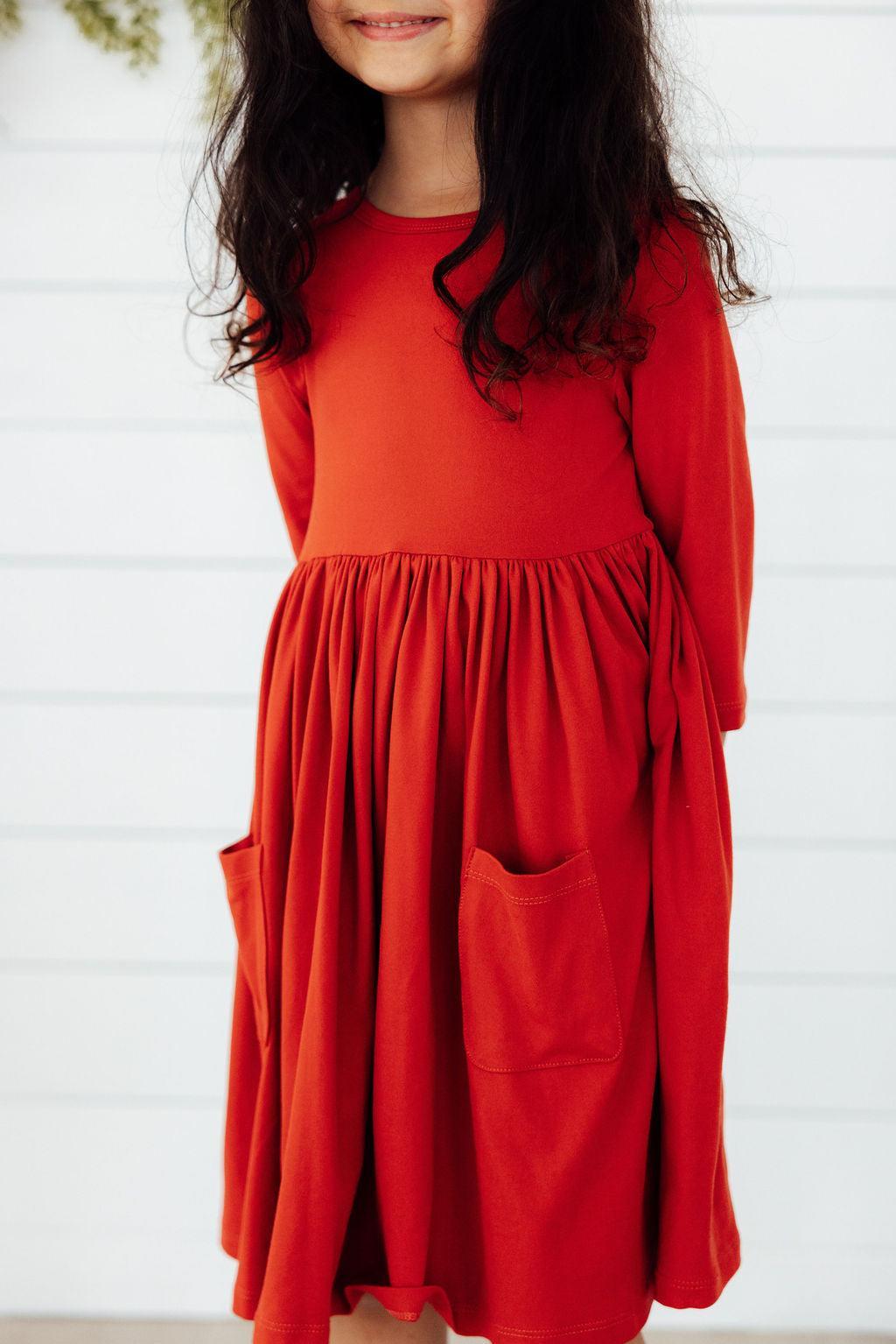 Pumpkin Spice 3/4 Sleeve Pocket Twirl Dress on a smiling girl, showcasing the vibrant autumn hue and playful pockets.