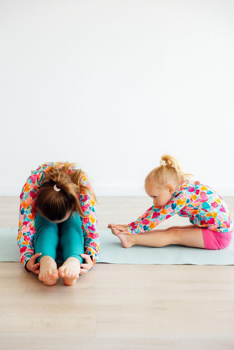 A mother and daughter in yoga poses, both wearing the Heart Hustle Full-Zip Ruffle Girls Active Jacket in Turbo Teal, highlighting the flexibility and style of these girls active jackets.