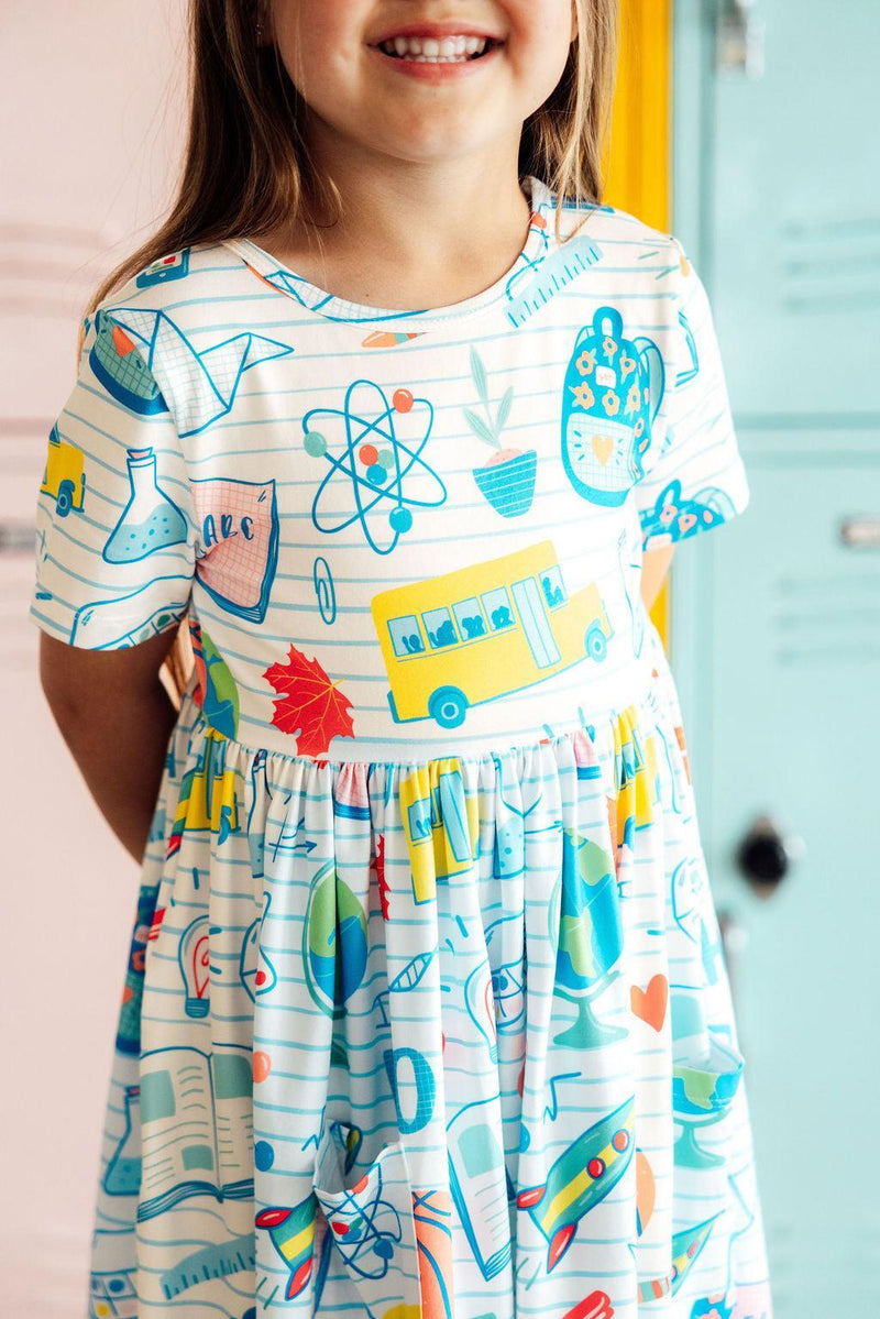 Close-up of a girl wearing the School Rules Short Sleeve Pocket Twirl Dress for Girls, featuring playful designs with school-themed graphics. This twirl dress for girls combines style and comfort for any activity.