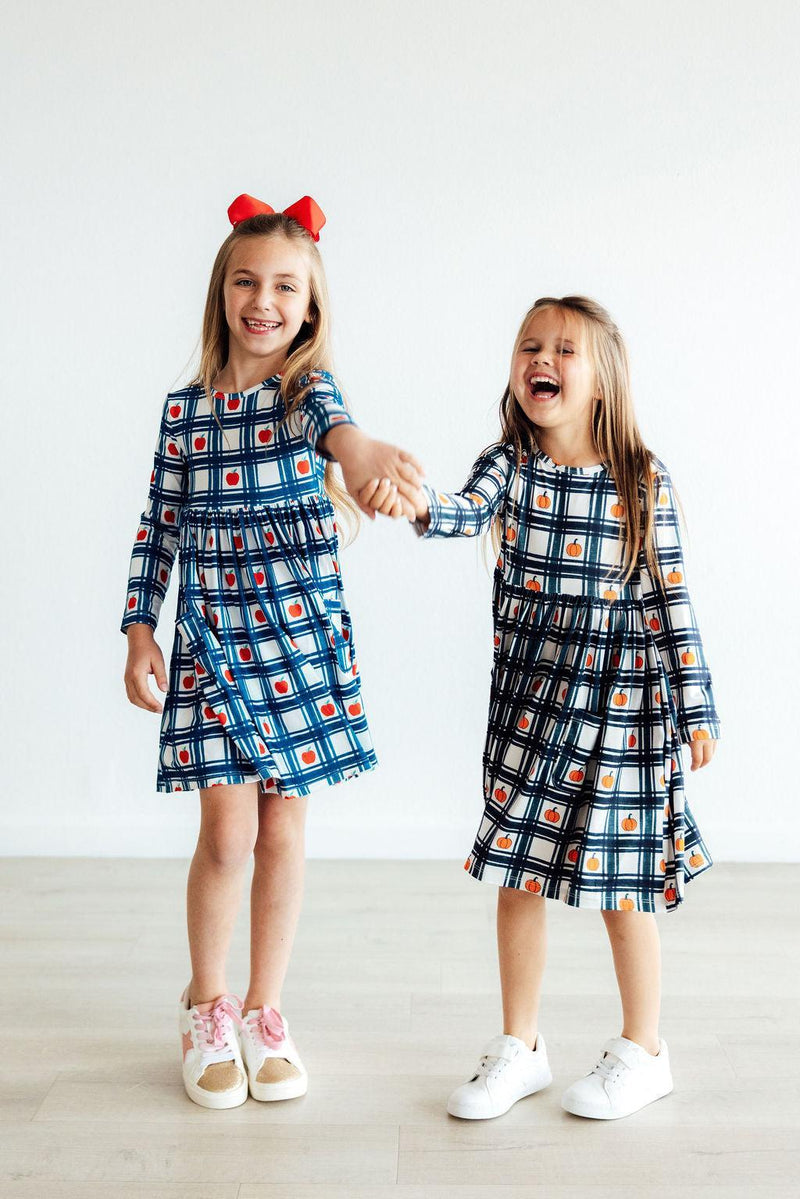 Two cheerful girls in matching Plaid Pumpkins Long Sleeve Pocket Twirl Dresses, holding hands and laughing, perfect for festive fun.