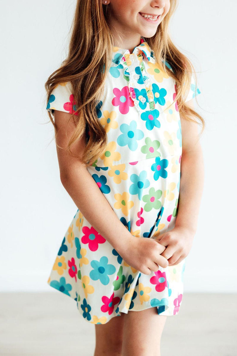 Close-up of a girl holding the skirt of the 'Groovy Blooms' Colorful Short Sleeve Girls Polo Dress, highlighting its playful floral design and comfortable fit. The ultimate girls polo dress for playful adventures.