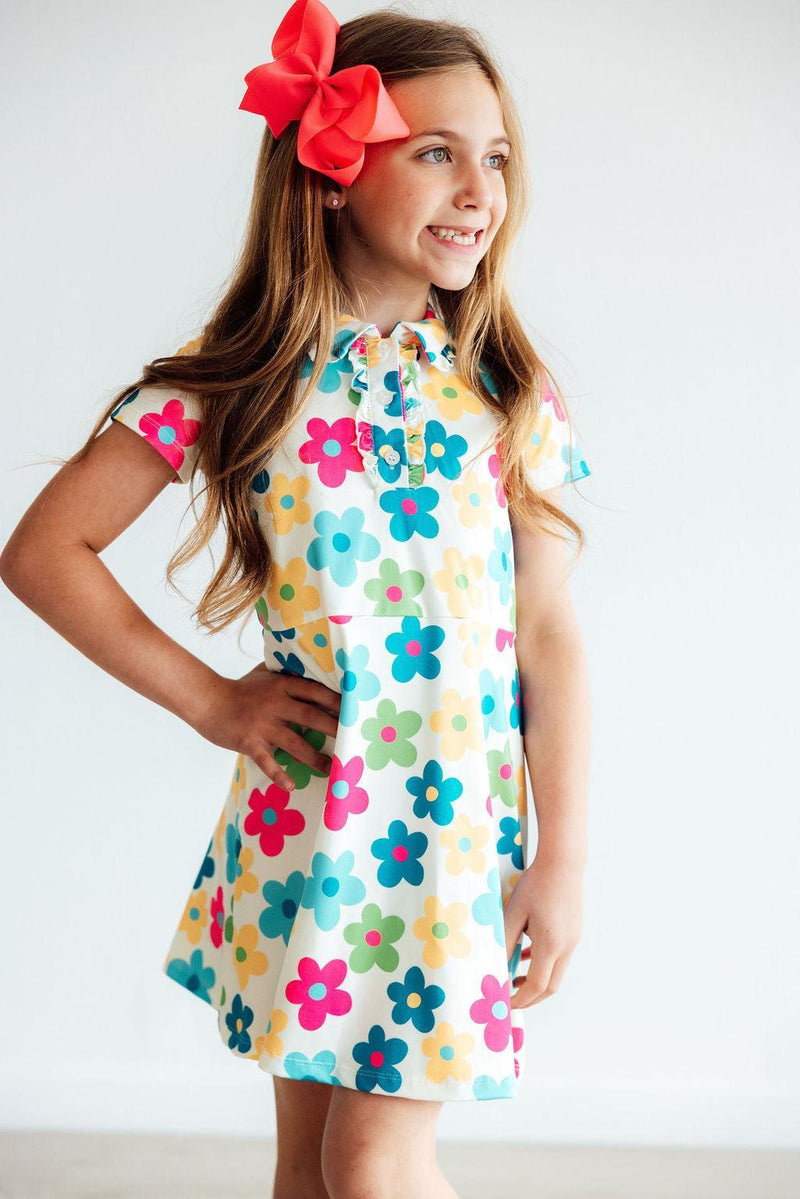 A charming girl posing in the 'Groovy Blooms' Colorful Short Sleeve Girls Polo Dress, featuring bright flowers and a youthful spirit. A stylish girls polo dress for every occasion.