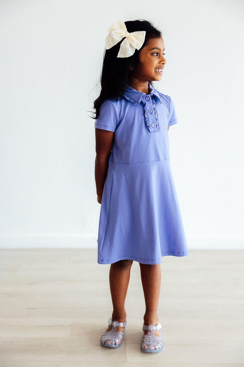 Delightful Periwinkle S/S Polo Dress worn by a young girl, featuring a ruffled collar and button placket, perfect for stylish playdates.